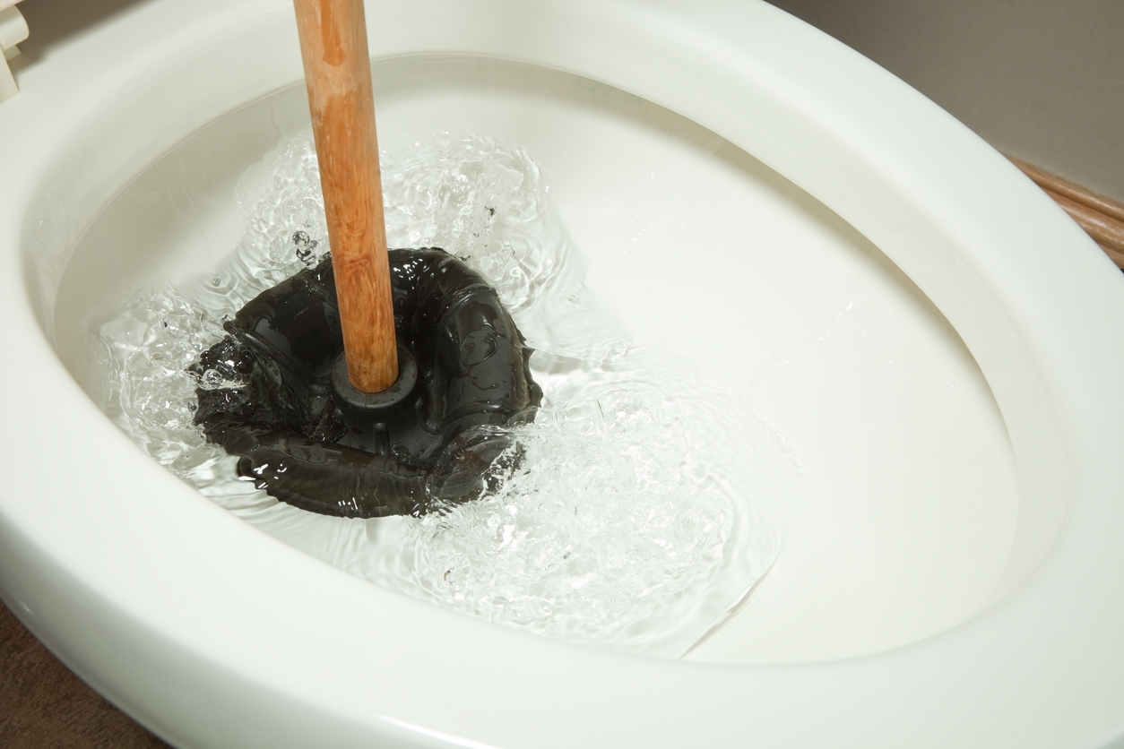 Plunger clearing a clogged toilet with water rising in the bowl.