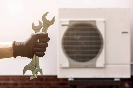Heat pump installation by repairman holding wrench outside.