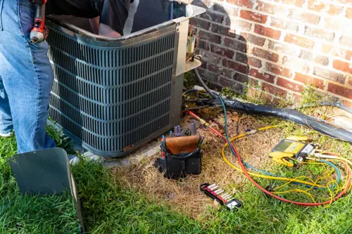 HVAC technician repairing an outdoor AC unit with gauges and tools for emergency air conditioning service in Charlotte.