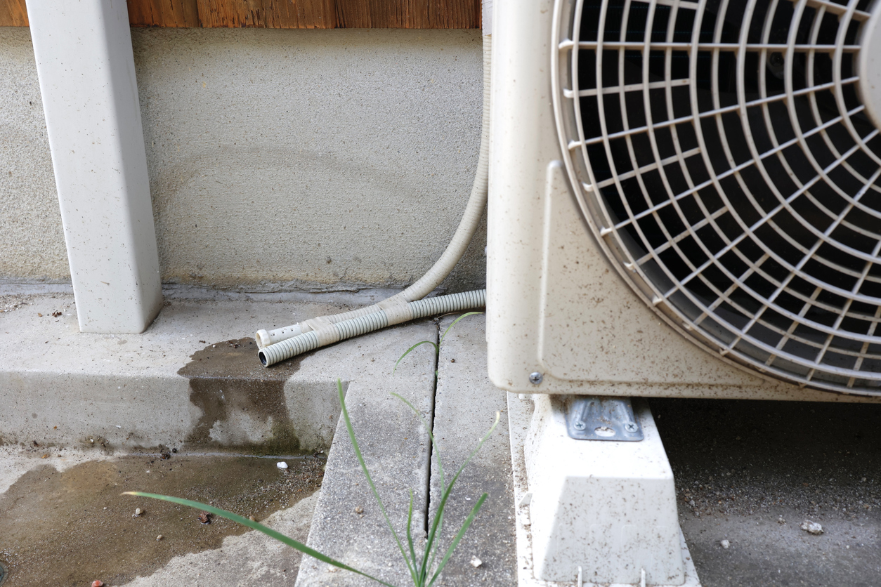 AC leak causing water to pool beside an outdoor air-conditioning unit and drain hose.