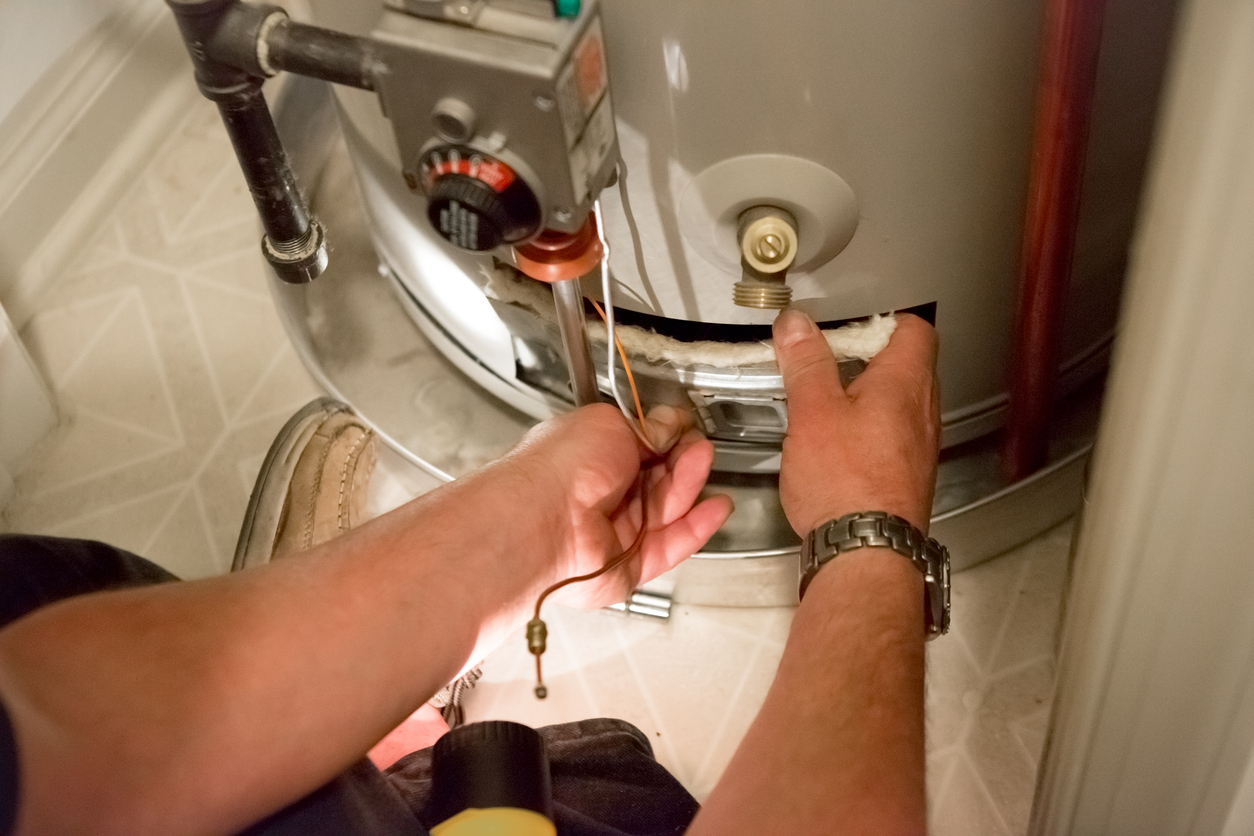 A man uses a flashlight to help him see the hot water heater in a dark closet.
